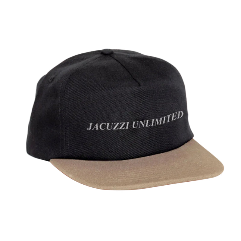 A black baseball cap with a beige flat brim, featuring the text 'JACUZZI UNLIMITED' embroidered in white on the front. The cap is shown against a solid coral pink background.