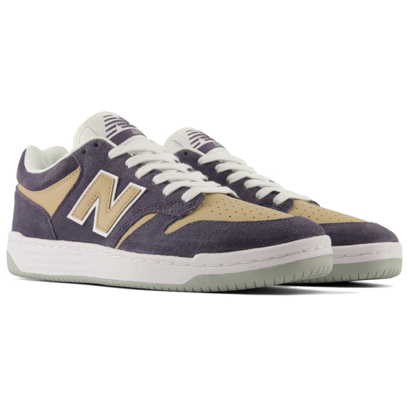 A pair of New Balance low-top skate shoes in a dark grey and beige colorway, featuring white laces and a white midsole with a light green outsole.