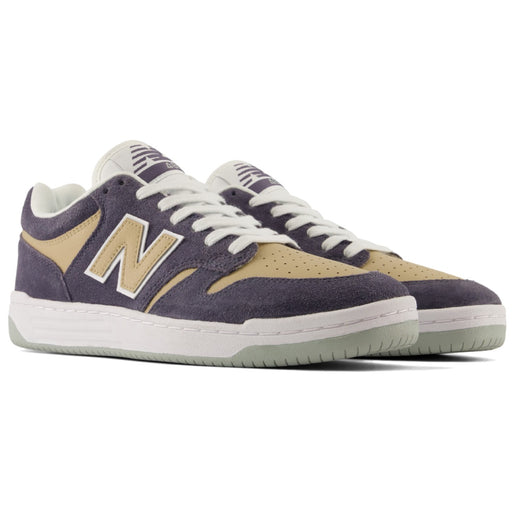 A pair of New Balance low-top skate shoes in a dark grey and beige colorway, featuring white laces and a white midsole with a light green outsole.