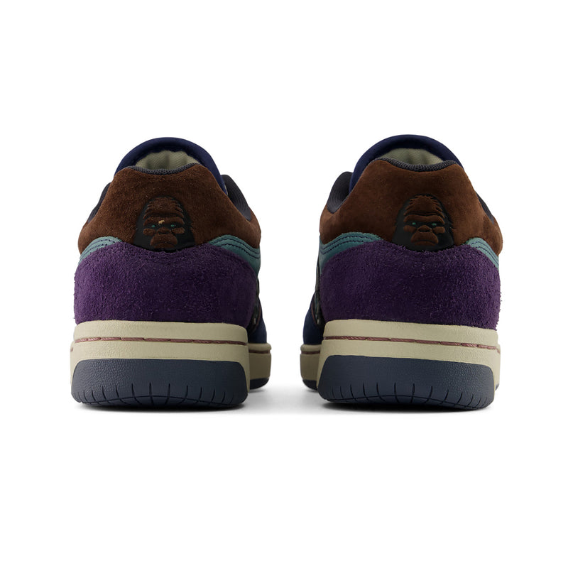 New Balance Numeric 480 x 35th North A pair of low-top sneakers shown from the back, featuring brown suede overlays, a purple suede heel section, a dark navy collar, a teal side stripe, and a cream midsole.