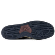 The outsole of a New Balance sneaker, showing a dark navy blue tread with a brown heel patch featuring the embossed New Balance 'N' logo.