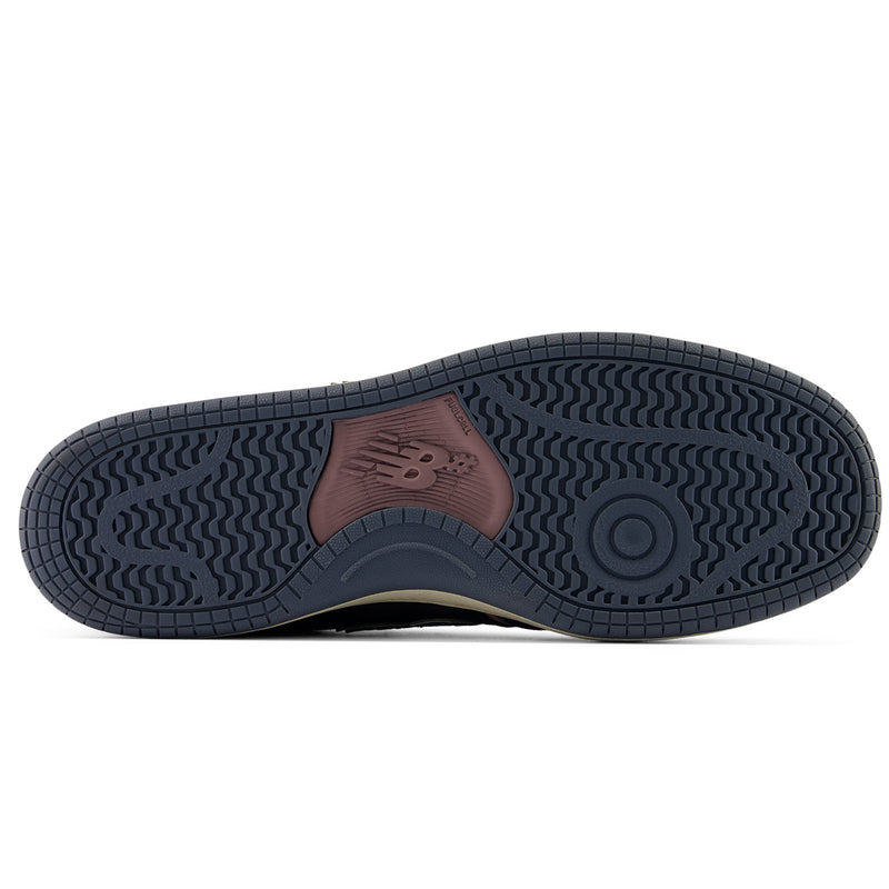 The outsole of a New Balance sneaker, showing a dark navy blue tread with a brown heel patch featuring the embossed New Balance 'N' logo.