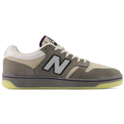 New Balance Numeric 480 x Civil sneaker in a muted gray and beige colorway with white laces, a purple accent line, and a translucent yellow-green gum sole, shown in a side profile on a white background.