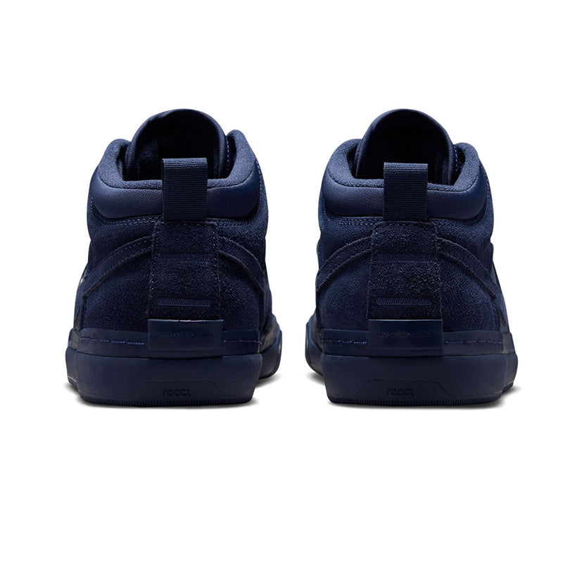 Nike SB React Leo - Navy/Navy A pair of navy blue mid-top sneakers shown from the back, featuring a textured suede and synthetic upper with pull tabs and thick navy soles