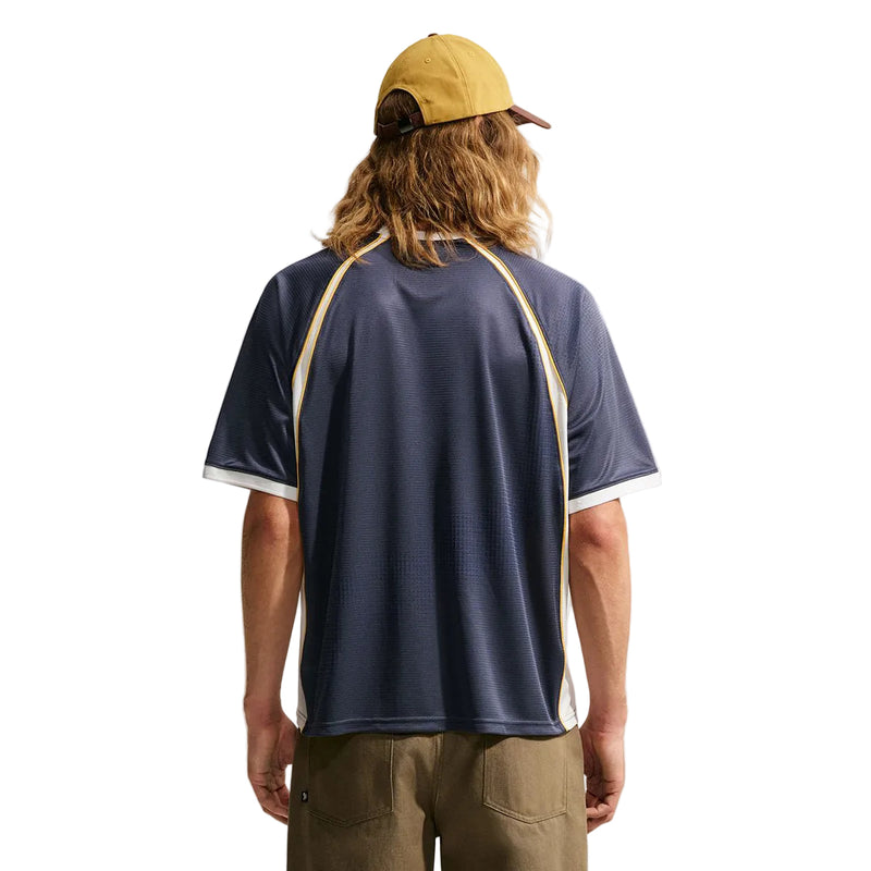 Nike SB x Yuto Jersey with beige and white contrast stitching, a yellow baseball cap, and khaki pants against a plain white background.