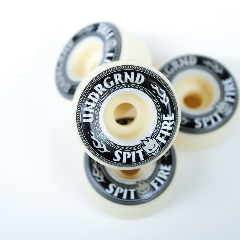 Four skateboard wheels stacked in a cluster on a clean white background, featuring cream-colored urethane and black outer rings with white text reading 'UNDGRND' and 'SPIT FIRE'.