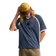  Nike SB x Yuto athletic jersey with white and orange accents, a yellow and brown baseball cap, and khaki pants, posed against a light gray studio background.