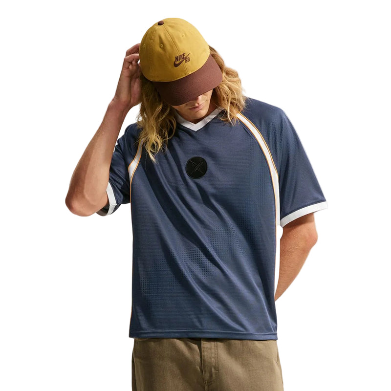  Nike SB x Yuto athletic jersey with white and orange accents, a yellow and brown baseball cap, and khaki pants, posed against a light gray studio background.